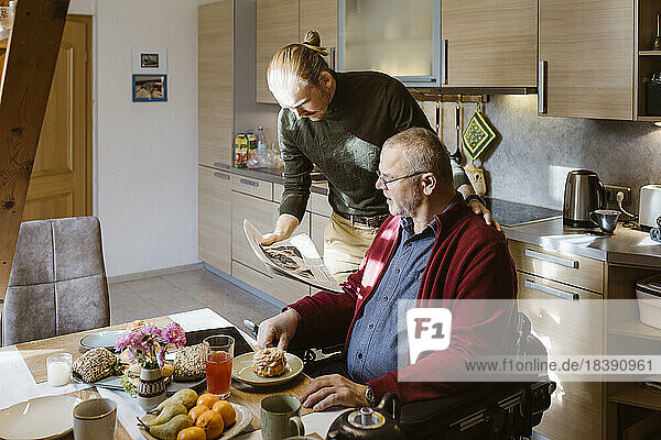 Junger Hausmeister teilt die Zeitung mit einem älteren Mann  während er zu Hause frühstückt