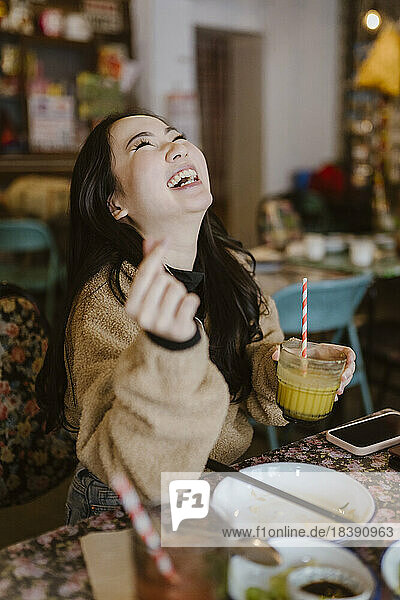 Junge Frau lacht und hält ein Getränk in einem Restaurant