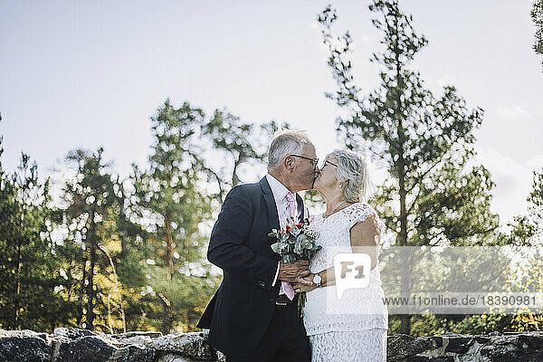 Zärtliches frisch verheiratetes älteres Paar küsst sich auf den Mund vor dem Wald am Hochzeitstag