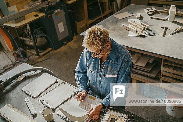 Blick von oben auf eine ältere Handwerkerin  die in einer Werkstatt an einem Dokument schreibt