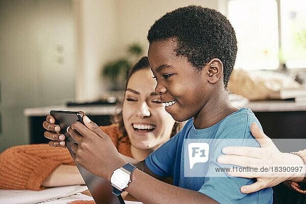 Glückliche Mutter mit Arm um Sohn genießt  während sie digitale Tablette zu Hause beobachten