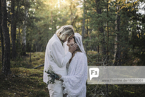 Newly married couple kissing in forest on wedding day