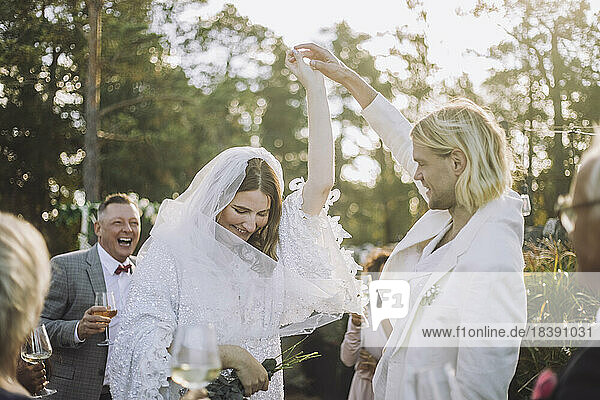 Glücklicher Bräutigam hält die Hand der Braut und tanzt inmitten der Gäste bei einer Hochzeitsfeier