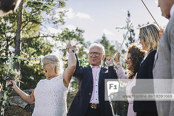 Glückliches Ehepaar hält sich an den Händen und tanzt mit der Familie bei der Hochzeitszeremonie