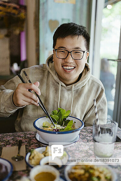 Porträt eines lächelnden jungen Mannes mit Essen und Stäbchen in einem Restaurant
