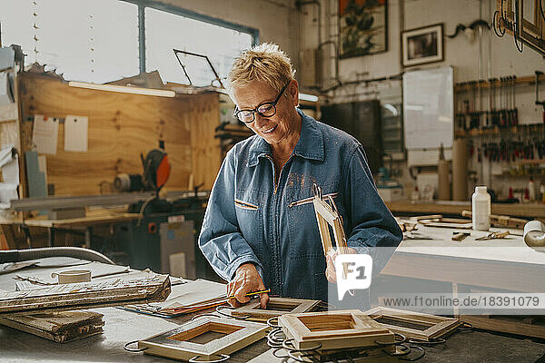 Lächelnder Senior-Tischler bei der Prüfung von Rahmen in der Werkstatt