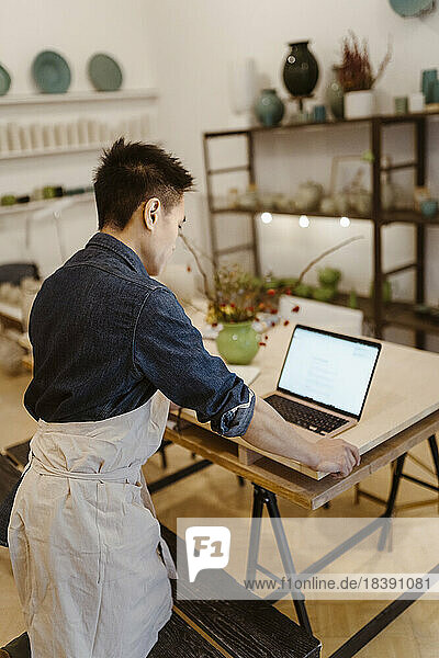 Männlicher Töpfer  der in der Werkstatt stehend am Laptop arbeitet