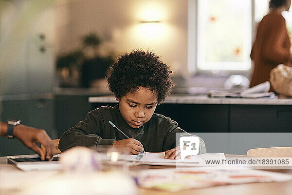 Boy with curly hair writing in book at home