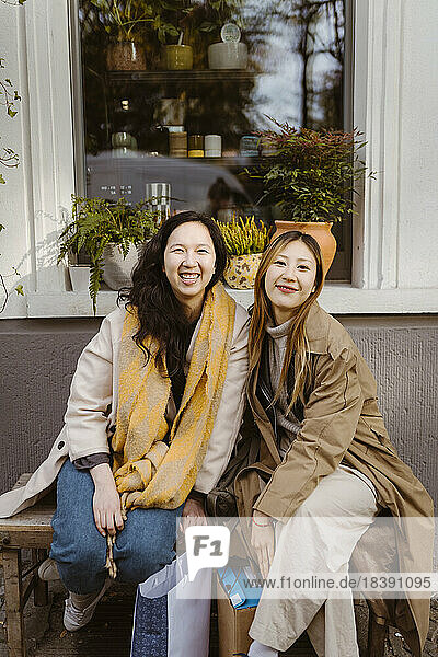 Portrait of happy female friends sitting together on bench