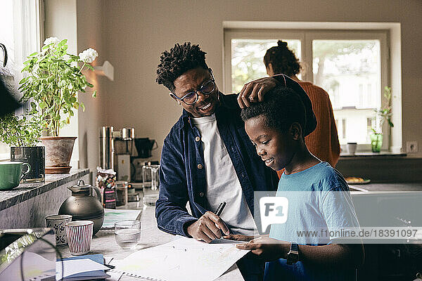 Smiling father caressing hair of son doing homework at home