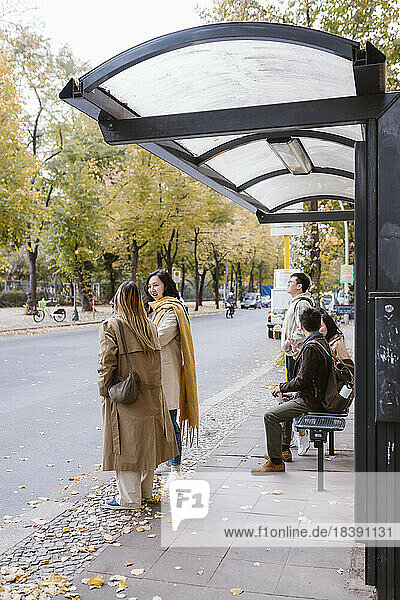 Männliche und weibliche Freunde unterhalten sich beim Warten an der Bushaltestelle