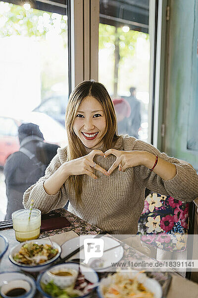 Portrait of happy woman making heart shape gesture while sitting at restaurant