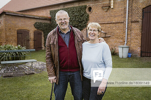 Porträt eines lächelnden älteren Mannes mit einem Arm um eine Frau  die an einem Haus im Hinterhof steht