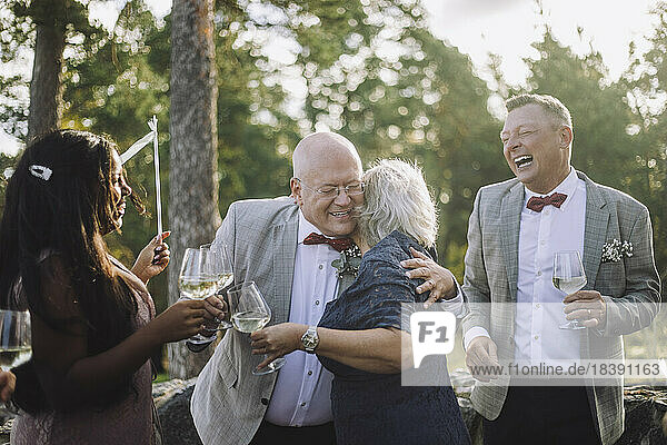 Glatzköpfiger älterer Bräutigam umarmt seine Freundin beim Weintrinken auf der Hochzeitsfeier