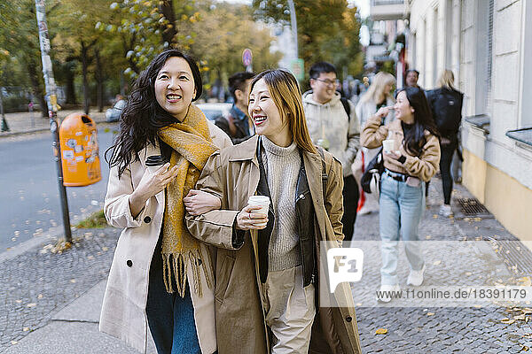 Lächelnde Freundinnen  die Arm in Arm auf dem Bürgersteig gehen