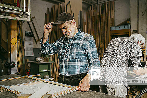 Älterer männlicher Tischler  der mit einem Kollegen in einer Reparaturwerkstatt eine Kappe einstellt
