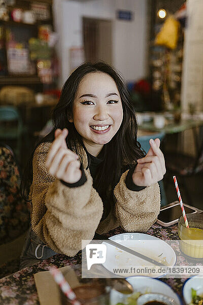 Porträt einer lächelnden Frau  die im Restaurant mit den Fingern ein Herz formt
