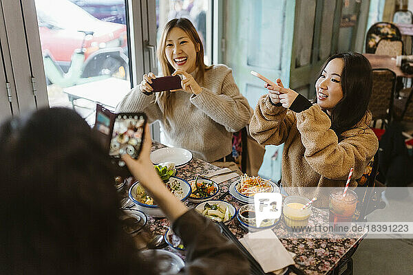 Happy female friends photographing food while sitting at restaurant