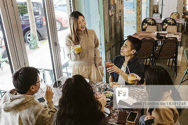 Lächelnde Frau genießt Getränke mit männlichen und weiblichen Freunden in einem Restaurant