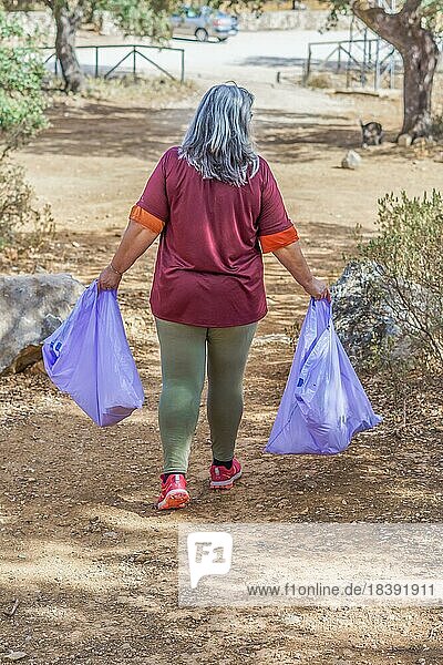 Frau von hinten gesehen  die Säcke mit auf dem Feld gesammeltem Müll trägt