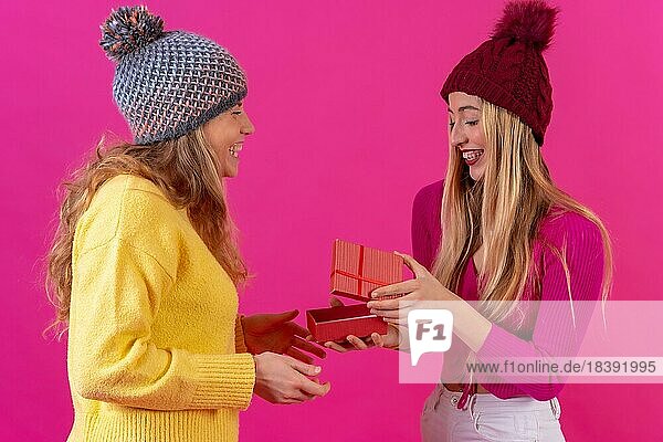 Zwei junge blonde kaukasische Frauen lächelnd Blick auf das Geschenk von der Freundin vor einem rosa Hintergrund