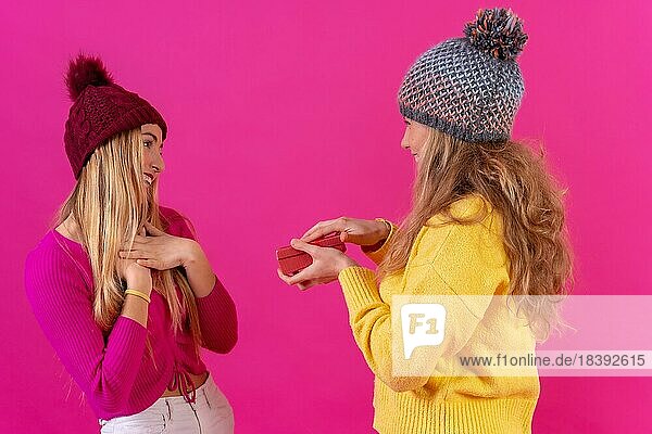 Zwei junge blonde kaukasische Frauen geben ein Geschenk in einer isolierten auf einem rosa Hintergrund
