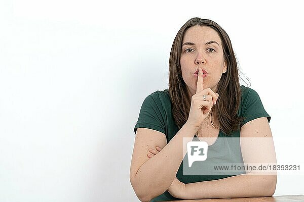 Close-up of young long-haired woman with finger in mouth asking for silence white background