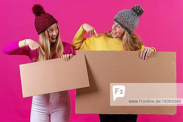 Zwei junge blonde kaukasische Frauen halten ein Schild vor einem rosa Hintergrund  Studioaufnahme  die auf