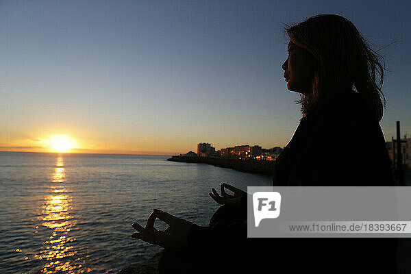Frau bei Yoga-Meditation am Meer bei Sonnenuntergang als Konzept für Ruhe und Entspannung  Cadiz  Andalusien  Spanien  Europa