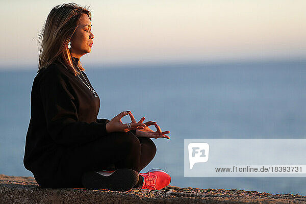 Frau bei einer Yoga-Meditation am Meer vor Sonnenuntergang als Konzept für Ruhe und Entspannung  Spanien  Europa