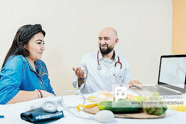 Lächelnder Ernährungsberater  der einer Patientin etwas erklärt  Ernährungsberater im Gespräch mit einer Patientin im Büro. Rückenansicht einer Patientin im Gespräch mit dem Ernährungsberater