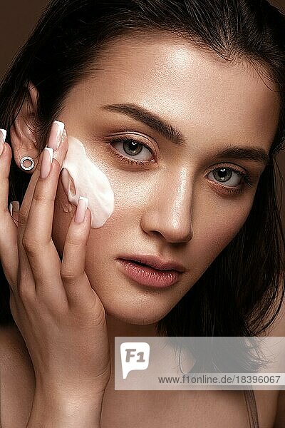 Beautiful young girl with natural nude make-up with cosmetics cream in hands. Beauty face. Photo taken in studio