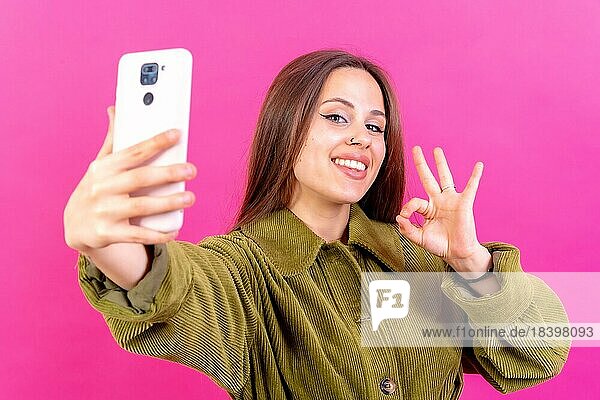 Isolierte Aufnahme einer kaukasischen Frau  die mit einer Handykamera ein Selfie macht und dabei die OkGeste macht