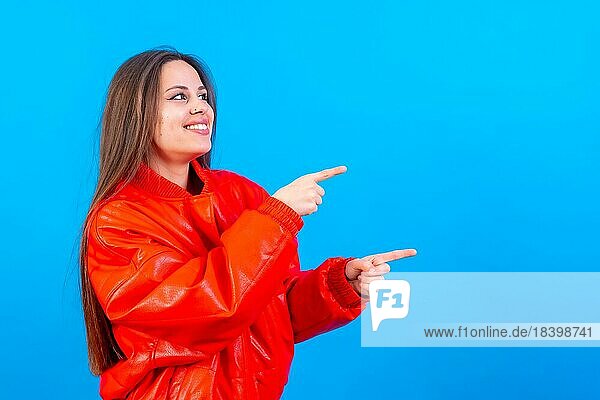 Attraktive Frau lächelnd Zeigefinger auf Kopie Raum auf blauem Hintergrund  rote Jacke sehr fröhlich