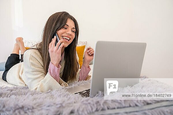 Frau arbeitet mit Laptop im Bett  Telearbeit  lächelnd am Telefon