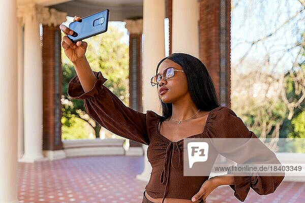 Eine schöne natürliche junge afrikanische Frau in einem Park. Lächelnd mit Sonnenbrille  die ein Selfie macht