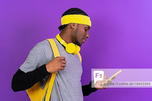 Schwarzer ethnischer Mann mit Rucksack und gelben Kopfhörern auf einem lila Hintergrund  Student Konzept