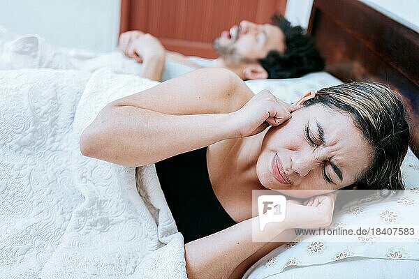 Ehefrau leidet unter dem Schnarchen ihres schlafenden Mannes. Schlafapnoe Konzept  Mann schnarcht im Schlafzimmer und Frau hält sich die Ohren zu