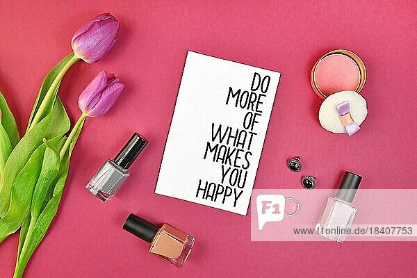 Happiness motivierendes Konzept mit Zeichen sagen Tun Sie mehr von dem  was Sie glücklich macht  umgeben von Frühlingsblumen und weibliche Accessoires wie Make up auf rosa Hintergrund  flach legen