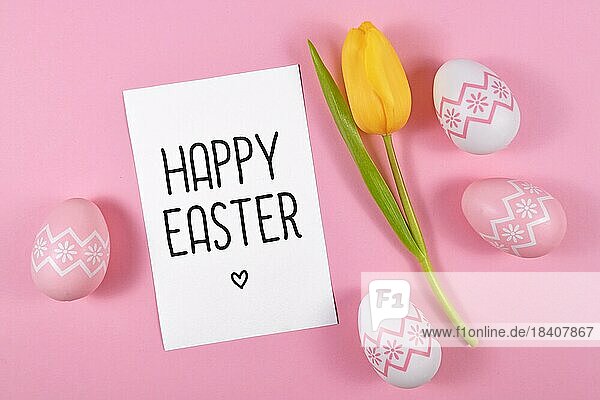 Frohe Ostern Textkarte durch Ostereier und einzelne gelbe Tulpe Frühlingsblume auf rosa farbigen Hintergrund umgeben  flach legen
