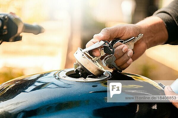 Hände  die den Benzintank des Motorrads mit dem Schlüssel öffnen. Hand öffnet den Gastank des Motorrads  Motorradfahrer öffnet den Gastank des Motorrads