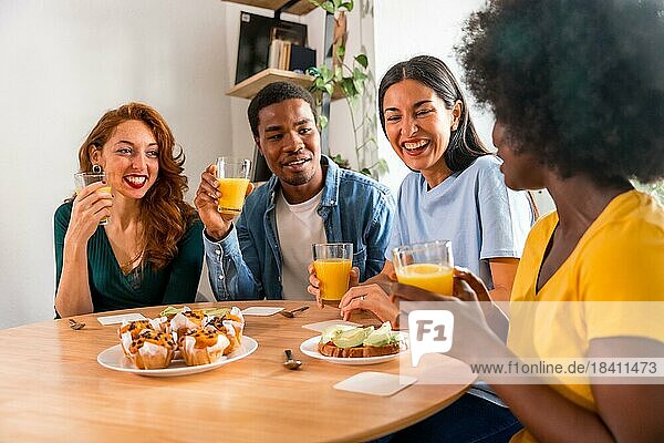 Multiethnische Freunde haben Spaß bei einem Frühstück mit Orangensaft und Muffins zu Hause