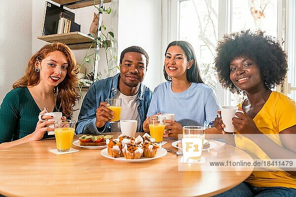 Multiethnic friends having breakfast with orange juice and muffins at home