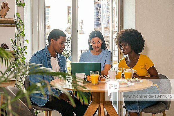Multiethnische Freunde beim Onlineshopping am Computer während des Frühstücks  am Fenster