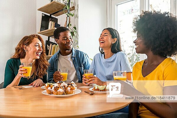 Multiethnische Freunde beim Frühstück mit Orangensaft und Muffins zu Hause