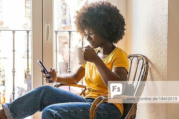Afrohaarige Frau am Fenster zu Hause mit einem heißen Getränk  Kaffee am Morgen