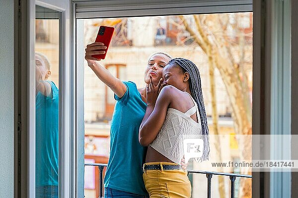 Beautiful lesbian couple embracing taking a selfie on the balcony at home  lgbt concept