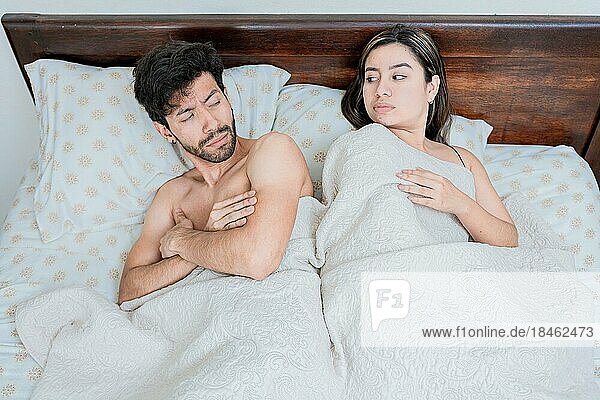 Upset couple in bed with crossed arms. Woman lying in bed upset with her husband. Angry man and woman in bed with crossed arms. Marriage problems concept
