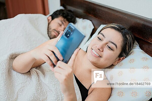Untreue Frau mit Telefon  während ihr Mann schläft. Untreue Frau mit Telefon  während der Mann schläft. Untreue Freundin mit Telefon  während der Freund schläft