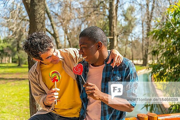 Paar multiethnische Männer  die einen Lutscher essen  lgbt Konzept  Spaß haben und lächelnd in einem Park